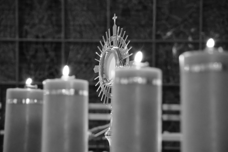 CZtery świece zapalone, za którymi znajduje się monstrancja z Najświętszym Sakramentem